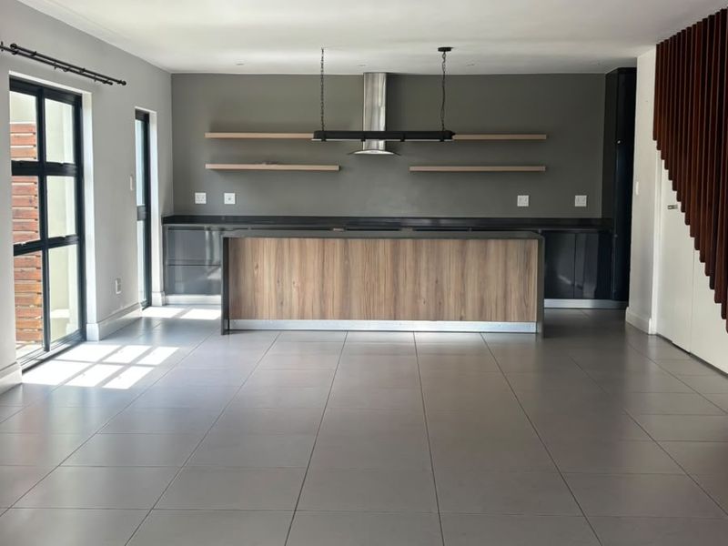 Spacious open-plan kitchen area featuring a modern island, sleek cabinetry, floating shelves, and contemporary tiled flooring, perfect for modern living.
