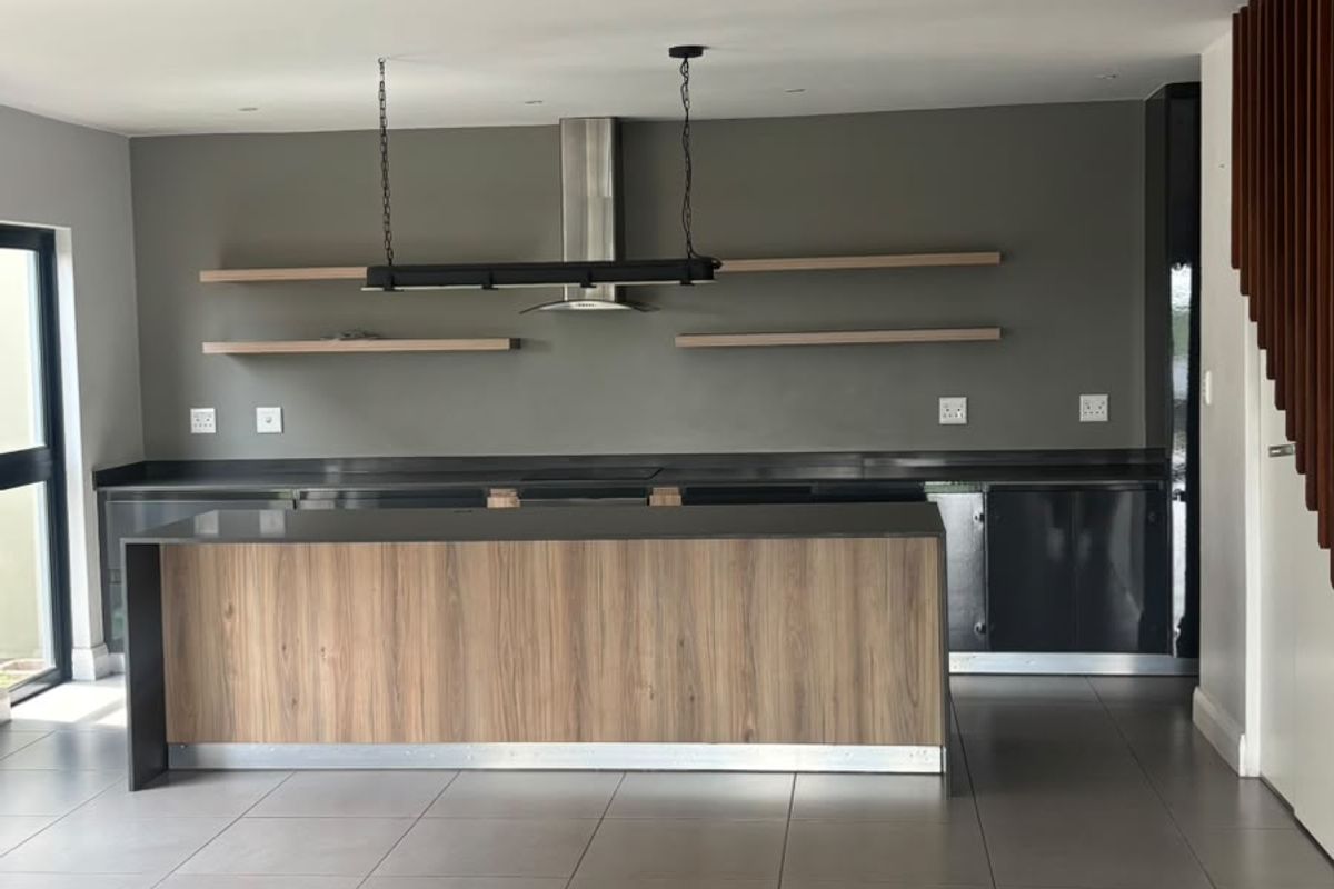 Modern kitchen featuring a central island, sleek cabinetry, floating shelves, and a stainless steel extractor fan, finished with neutral floor tiles.