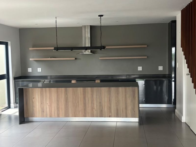 Modern kitchen featuring a central island, sleek cabinetry, floating shelves, and a stainless steel extractor fan, finished with neutral floor tiles.