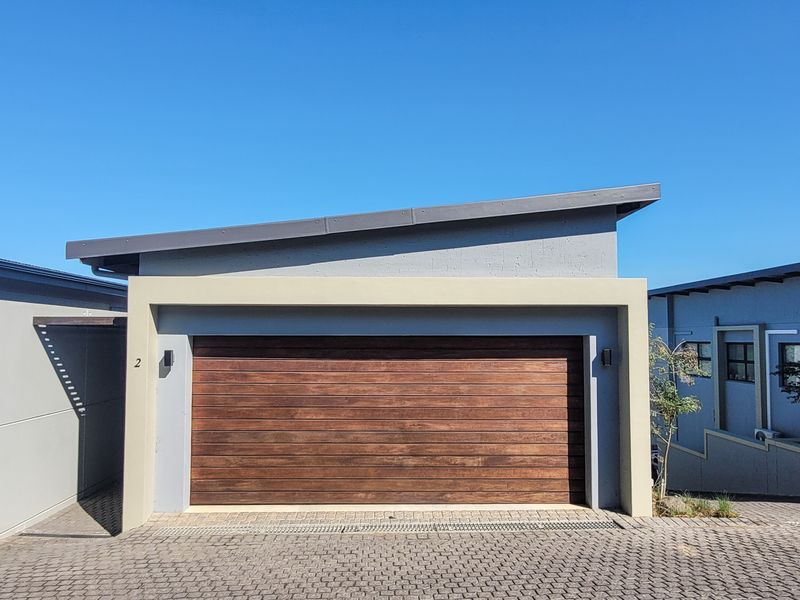 A modern townhouse garage featuring a timber-look sectional door, paved driveway, and contemporary skillion roof design.