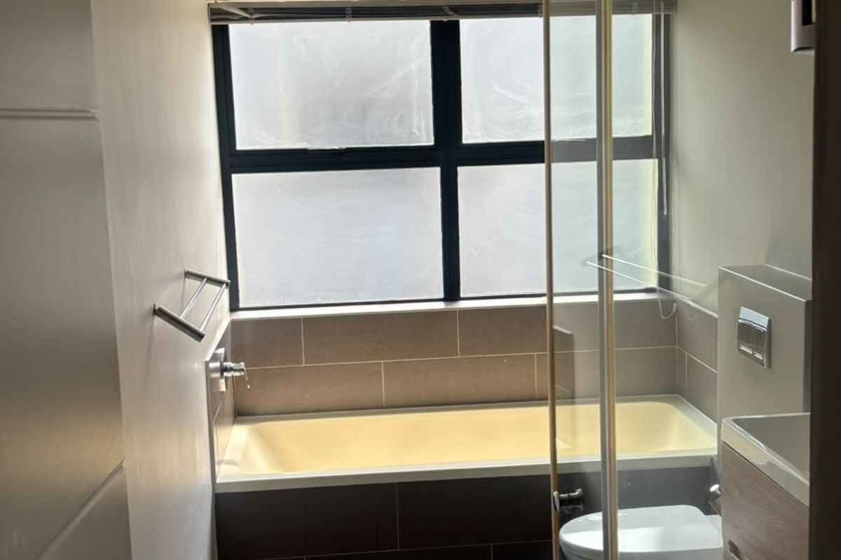 A modern, well-maintained bathroom featuring a built-in bathtub, glass-enclosed shower, wall-mounted toilet, and a sleek vanity cabinet with neutral tiling.