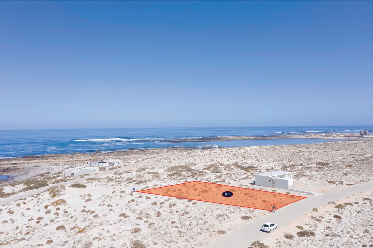 An aerial view of a vacant residential plot located in a coastal area, featuring direct road access and proximity to the ocean.