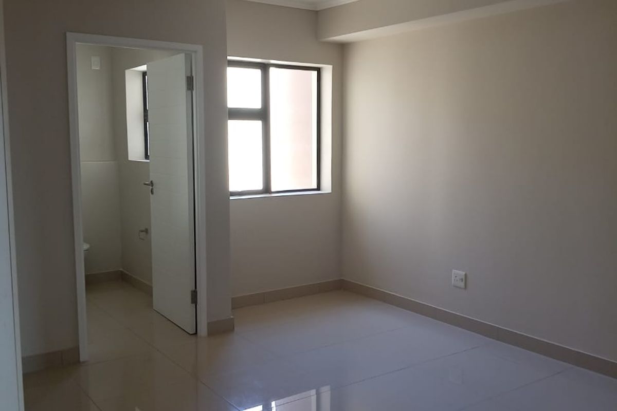 A bright, empty bedroom featuring neutral walls, polished tiled flooring, and an adjoining en-suite bathroom.