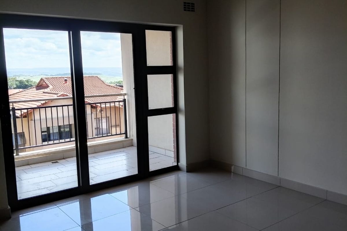 A bright, empty living area featuring large format floor tiles, recessed lighting, and sliding glass doors that open onto a private balcony.
