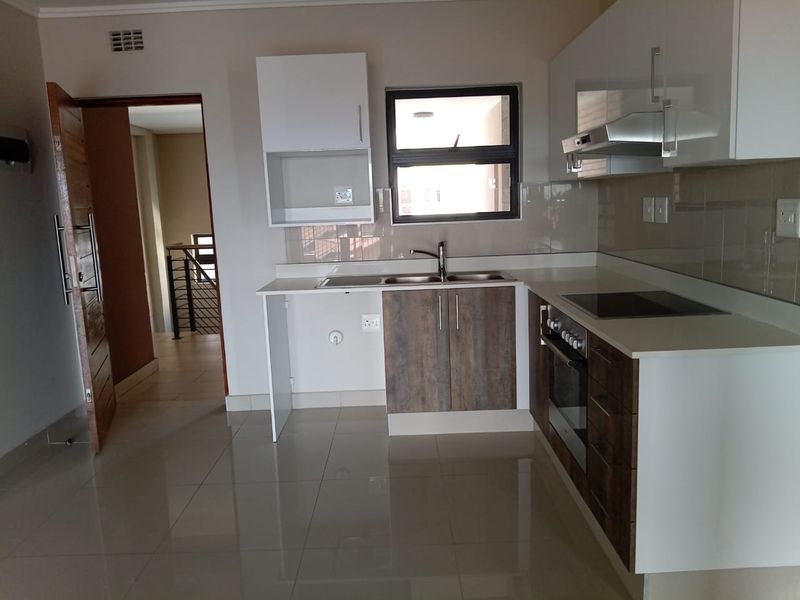 Modern kitchen featuring two-tone cabinetry, integrated electric hob and oven, stainless steel sink, and neutral tiled flooring in an open-plan layout.