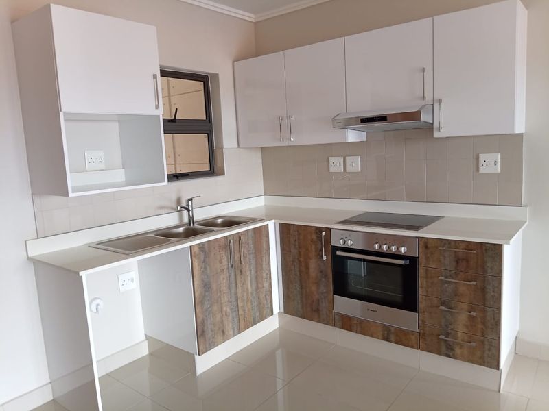Modern kitchen featuring sleek white and wood-grain cabinetry, stone countertops, integrated oven, electric hob, extractor fan, and tiled flooring.