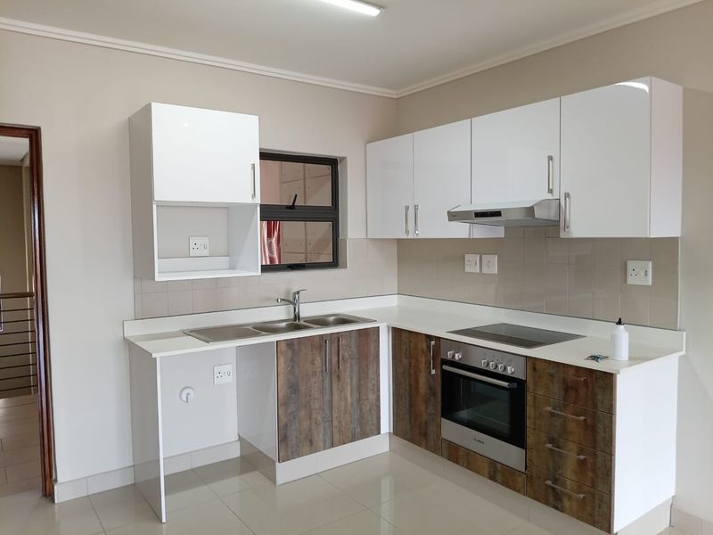 Modern kitchen featuring white upper cabinets, wood-look lower cabinetry, stone countertops, integrated oven, hob, and extractor fan with a tiled splashback.