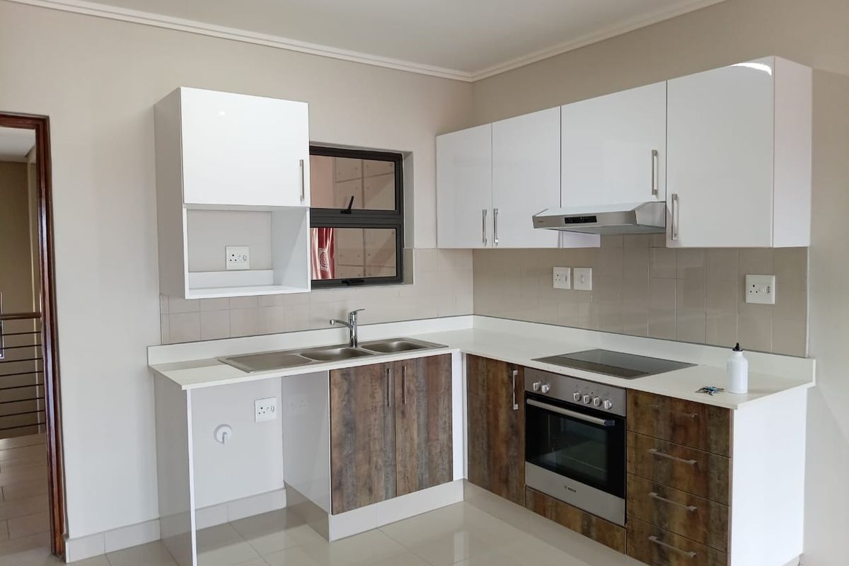Modern kitchen featuring white upper cabinets, wood-look lower cabinetry, stone countertops, integrated oven, hob, and extractor fan with a tiled splashback.