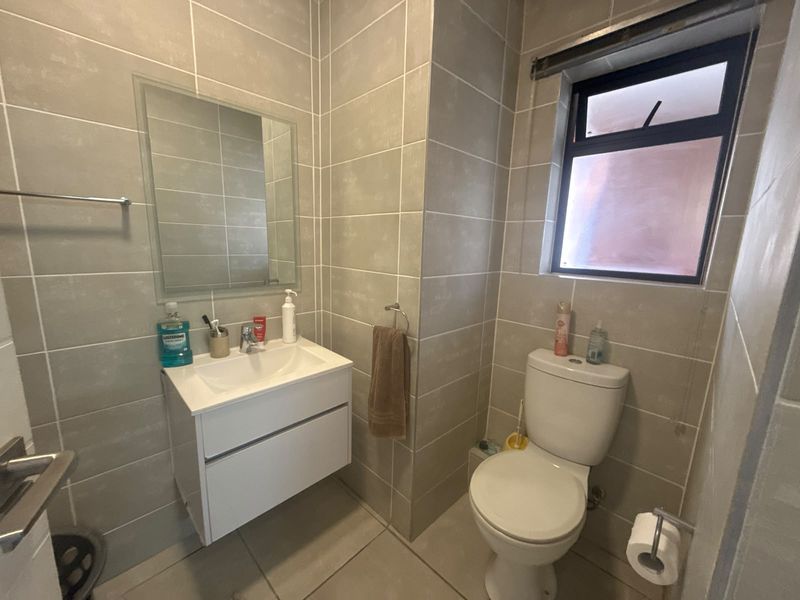 A modern bathroom featuring neutral wall-to-floor tiling, a wall-mounted vanity with a basin, and a functional toilet.