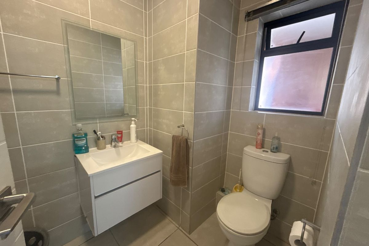 A modern bathroom featuring neutral wall-to-floor tiling, a wall-mounted vanity with a basin, and a functional toilet.