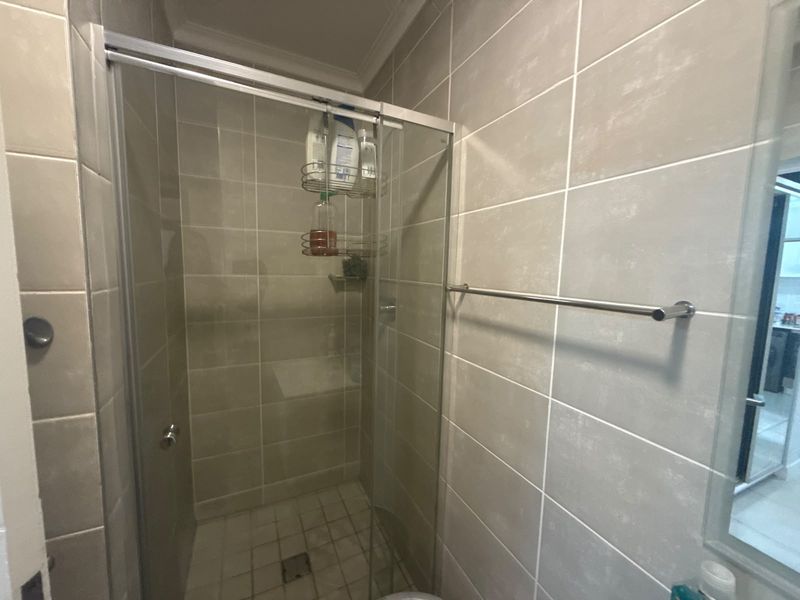 A clean bathroom featuring a glass-enclosed shower with neutral wall tiling and a wall-mounted towel rail.