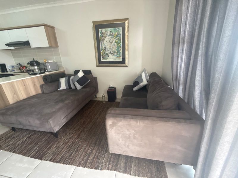 Open plan living area featuring tiled flooring and a compact kitchen with modern cabinetry and a tiled backsplash.