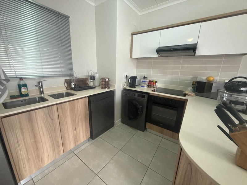 Modern kitchen featuring wood-finish cabinetry, stone countertops, integrated dishwasher, built-in oven with hob, and a double sink with tiled backsplash.
