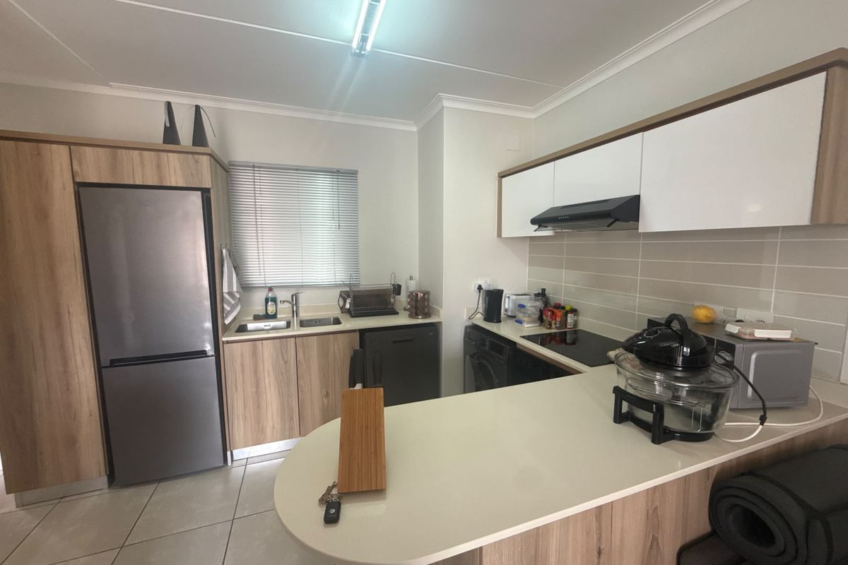 Modern kitchen featuring light wood-tone cabinetry, stone countertops, integrated appliances, and a breakfast bar, complemented by neutral tiled flooring and backsplash.