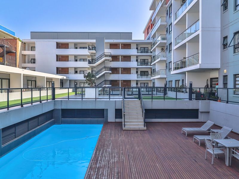 A well-maintained communal pool area featuring timber decking, glass balustrades, and direct access to the surrounding apartment complex.