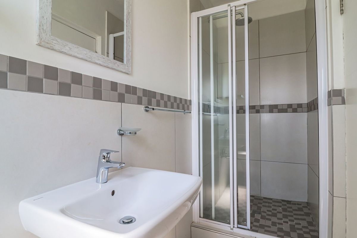 A clean and functional bathroom featuring a wall-mounted basin with chrome mixer tap and a separate shower enclosure with tiled finishes.