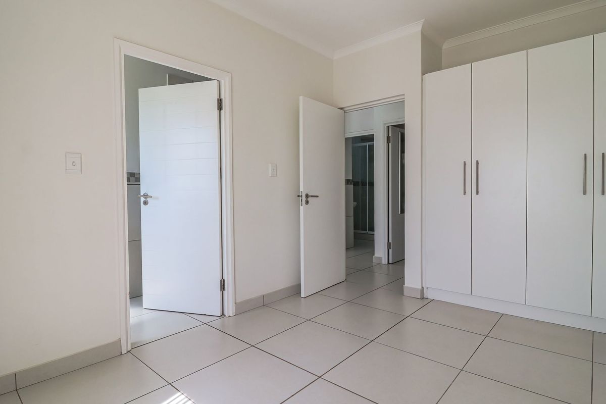 A bright, empty bedroom featuring neutral tiled flooring, built-in white cupboards, and access to an en-suite bathroom.
