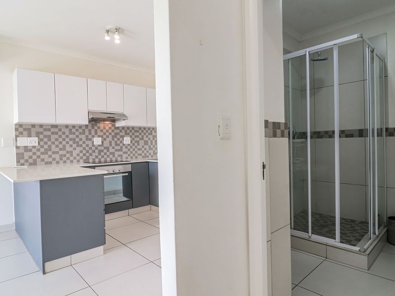 An open-plan apartment interior featuring a modern kitchen with built-in appliances and an adjacent bathroom with a glass shower and wall-mounted toilet.