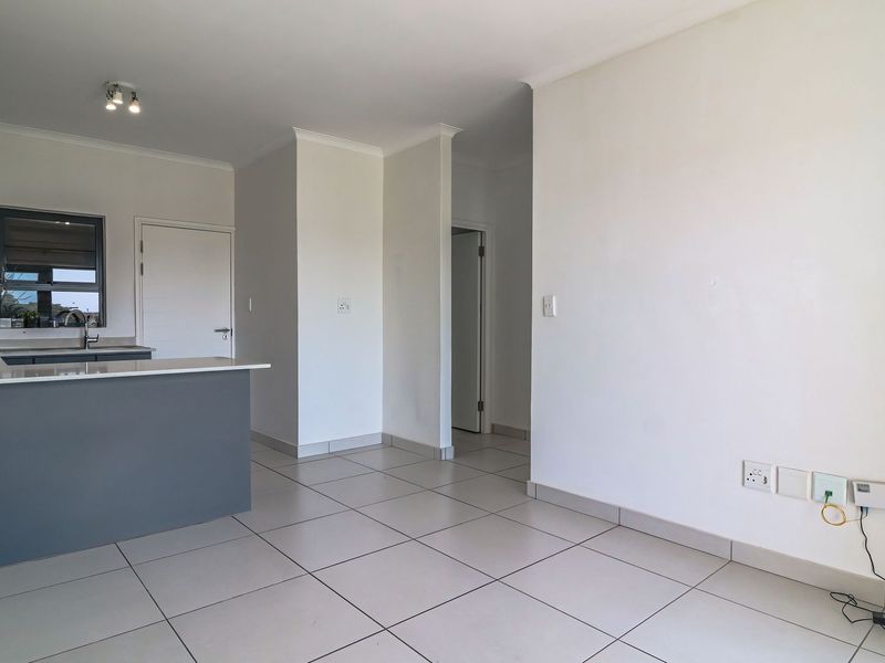 An open-plan living and kitchen area featuring modern cabinetry, stone countertops, and neutral tiled flooring in a clean, well-maintained space.