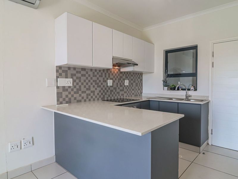 Modern kitchen featuring sleek two-tone cabinetry, stone countertops, mosaic tile backsplash, integrated hob, and extractor fan, finished with neutral tiled flooring.