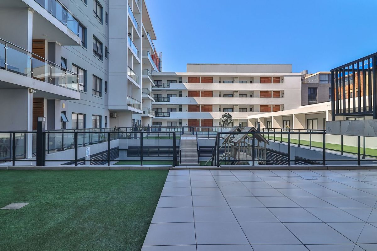 A view of the apartment complex courtyard featuring a tiled patio area, artificial lawn, and modern multi-story building facades with glass balustrades.
