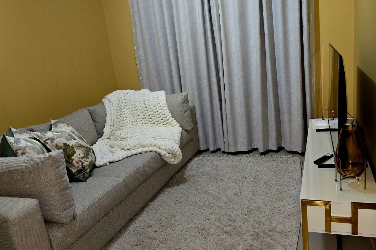 A cozy living room featuring neutral tiled flooring, mustard-toned walls, and floor-to-ceiling curtains, creating a warm and inviting atmosphere.