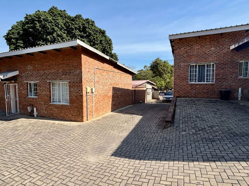 Exterior view of a brick apartment complex featuring a paved driveway, security window bars, and metal roofing.