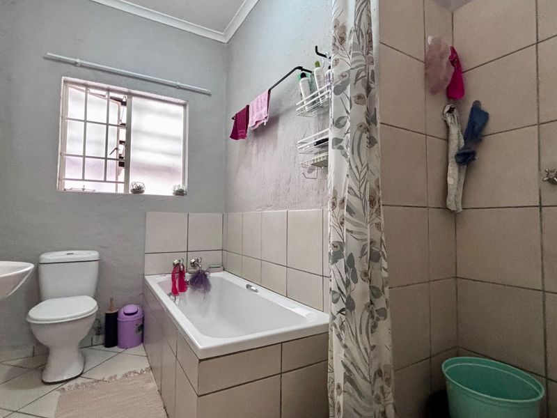 A functional bathroom featuring a bathtub, pedestal basin, and toilet with tiled finishes and a window with security bars.