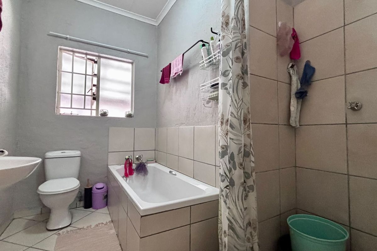 A functional bathroom featuring a bathtub, pedestal basin, and toilet with tiled finishes and a window with security bars.