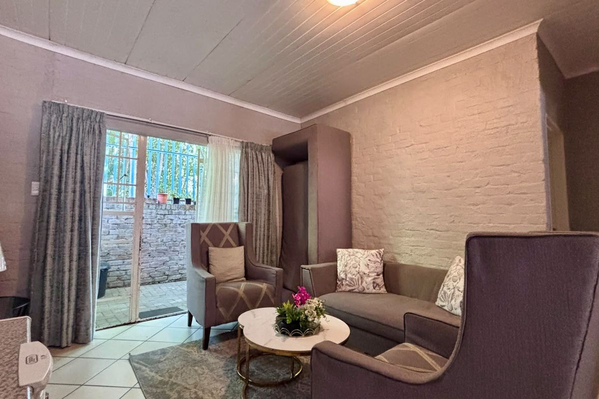 A cozy living room featuring a painted brick wall, tiled flooring, and a sliding glass door providing access to an outdoor patio area.