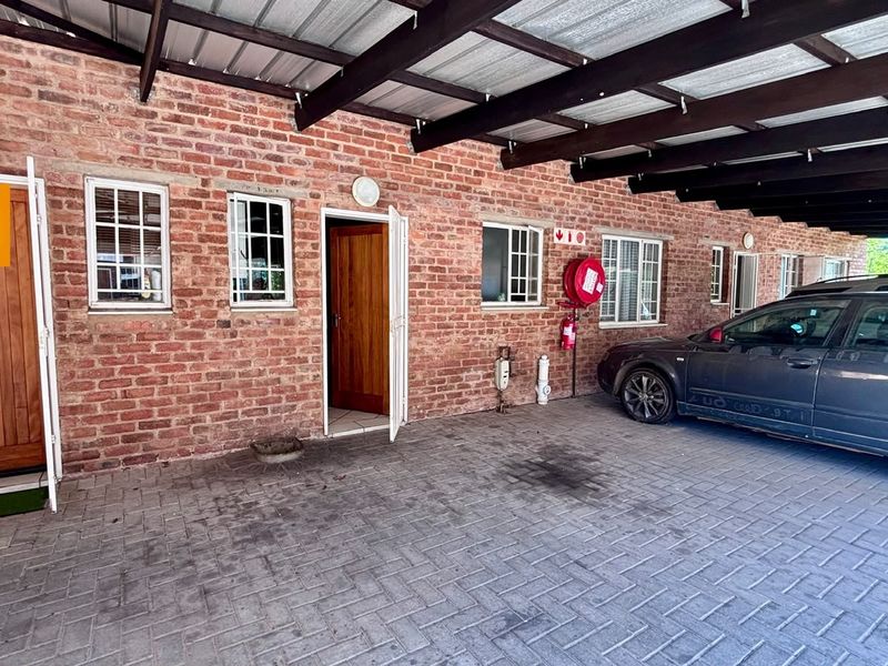 Exterior view of an apartment unit featuring an exposed brick facade, covered carport parking, and timber entrance doors.