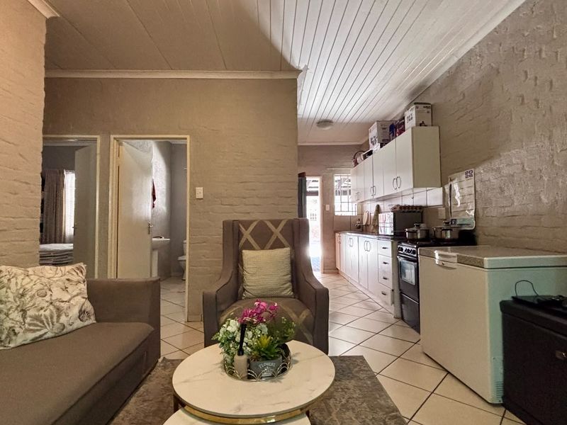 Open-plan living and kitchen area featuring exposed brick walls, tiled flooring, and functional built-in cabinetry with a tongue and groove ceiling.