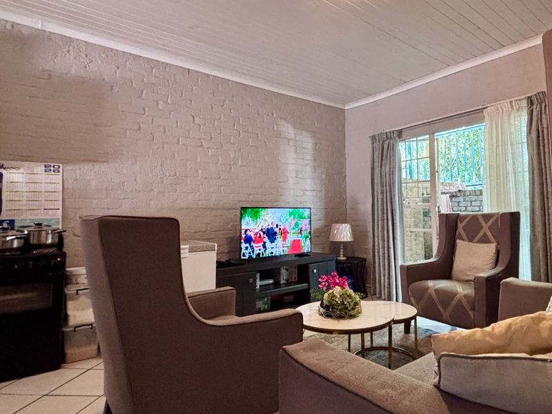 Open-plan living area featuring an exposed brick wall, timber panel ceiling, tiled floors, and direct access to an outdoor space via sliding glass doors.