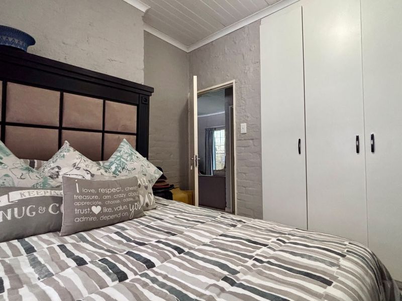 A bedroom featuring built-in cupboards, a textured painted brick wall, and a classic tongue and groove ceiling.