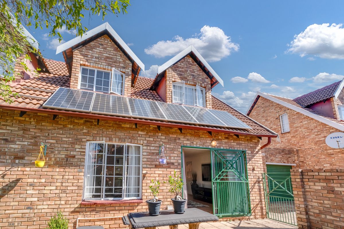 Rear view of a face-brick townhouse featuring a tiled roof, installed solar panels, and a secure entrance gate.