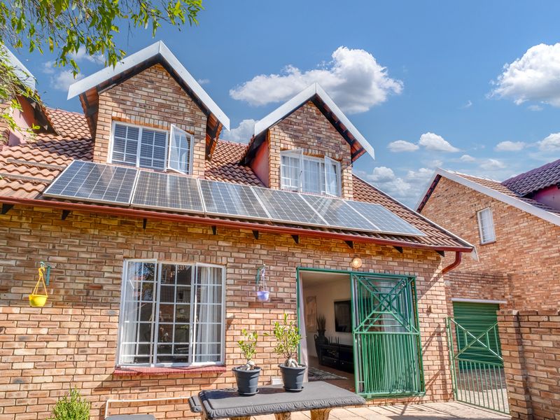 Rear view of a face-brick townhouse featuring a tiled roof, installed solar panels, and a secure entrance gate.