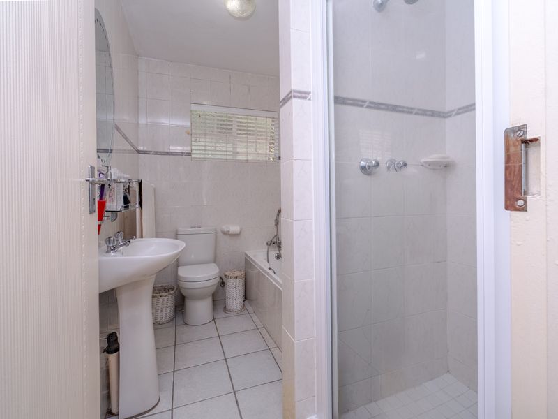 A functional bathroom featuring a pedestal basin, toilet, bathtub, and a separate shower enclosure with tiled finishes throughout.