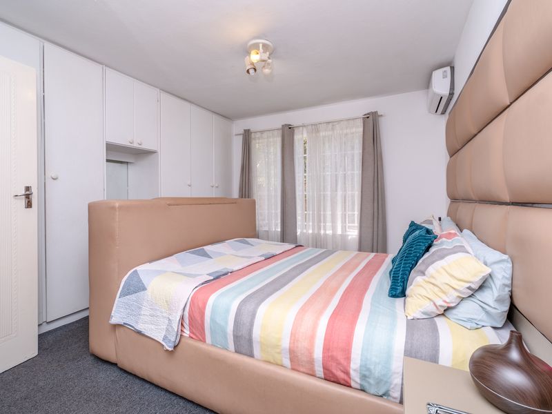 A well-maintained bedroom featuring built-in cupboards, carpeted flooring, and a wall-mounted split-system air conditioner for climate control.
