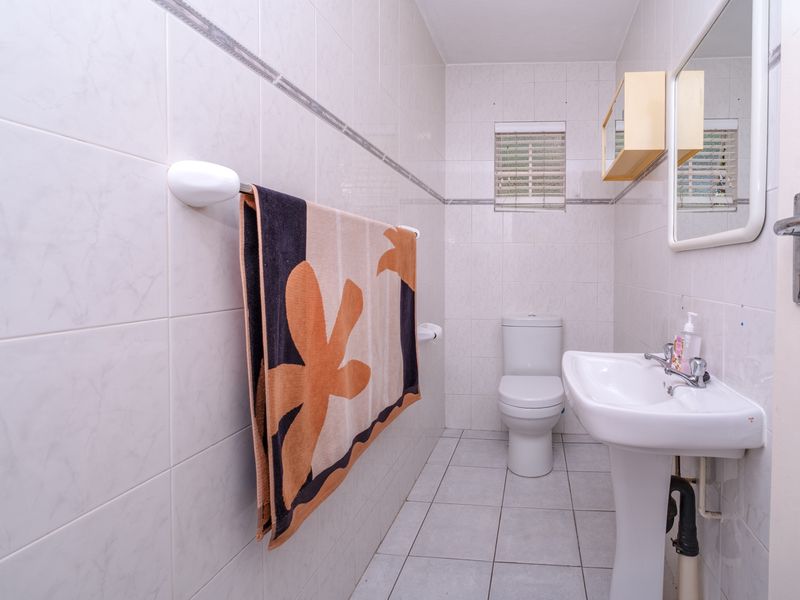 A functional bathroom featuring tiled walls and flooring, a pedestal basin, and a standard toilet.