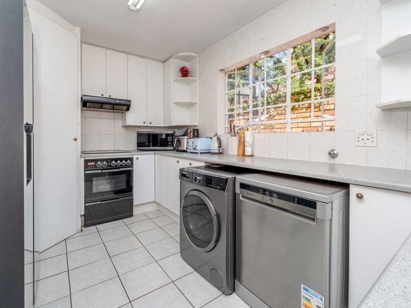 Functional kitchen featuring white cabinetry, tiled backsplash, built-in oven with extractor fan, and dedicated space for laundry appliances under the countertop.