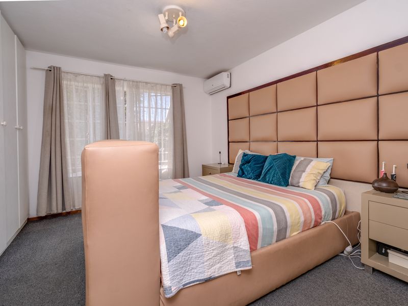 A well-maintained bedroom featuring built-in cupboards, a wall-mounted air conditioning unit, and a decorative upholstered headboard wall panel.