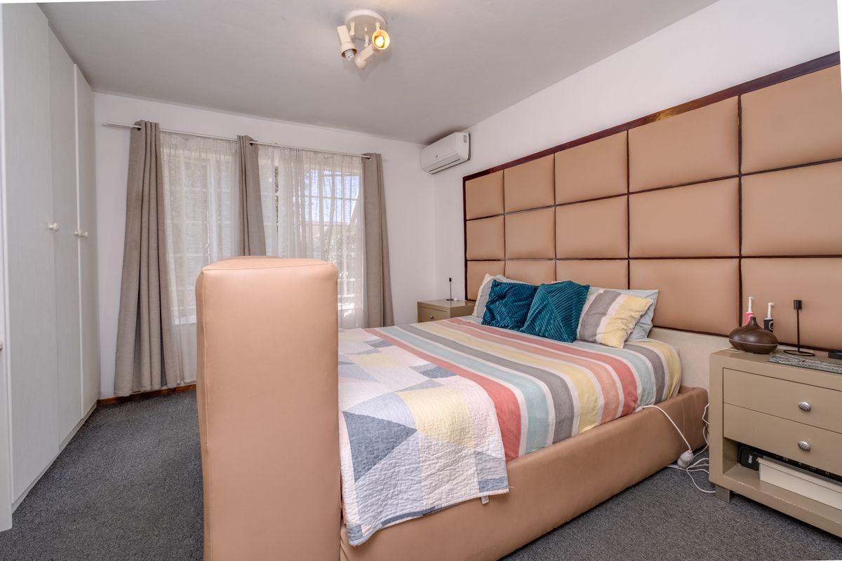 A well-maintained bedroom featuring built-in cupboards, a wall-mounted air conditioning unit, and a decorative upholstered headboard wall panel.