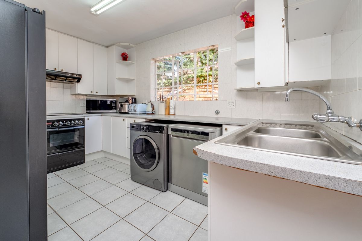 Functional kitchen featuring white cabinetry, laminate countertops, stainless steel sink, built-in oven, and tiled flooring with a window overlooking the exterior.