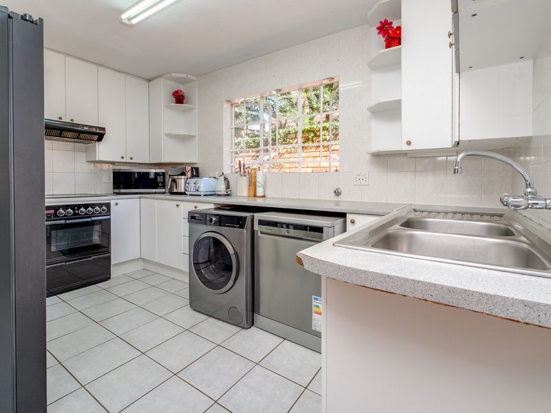 Functional kitchen featuring white cabinetry, laminate countertops, stainless steel sink, built-in oven, and tiled flooring with a window overlooking the exterior.