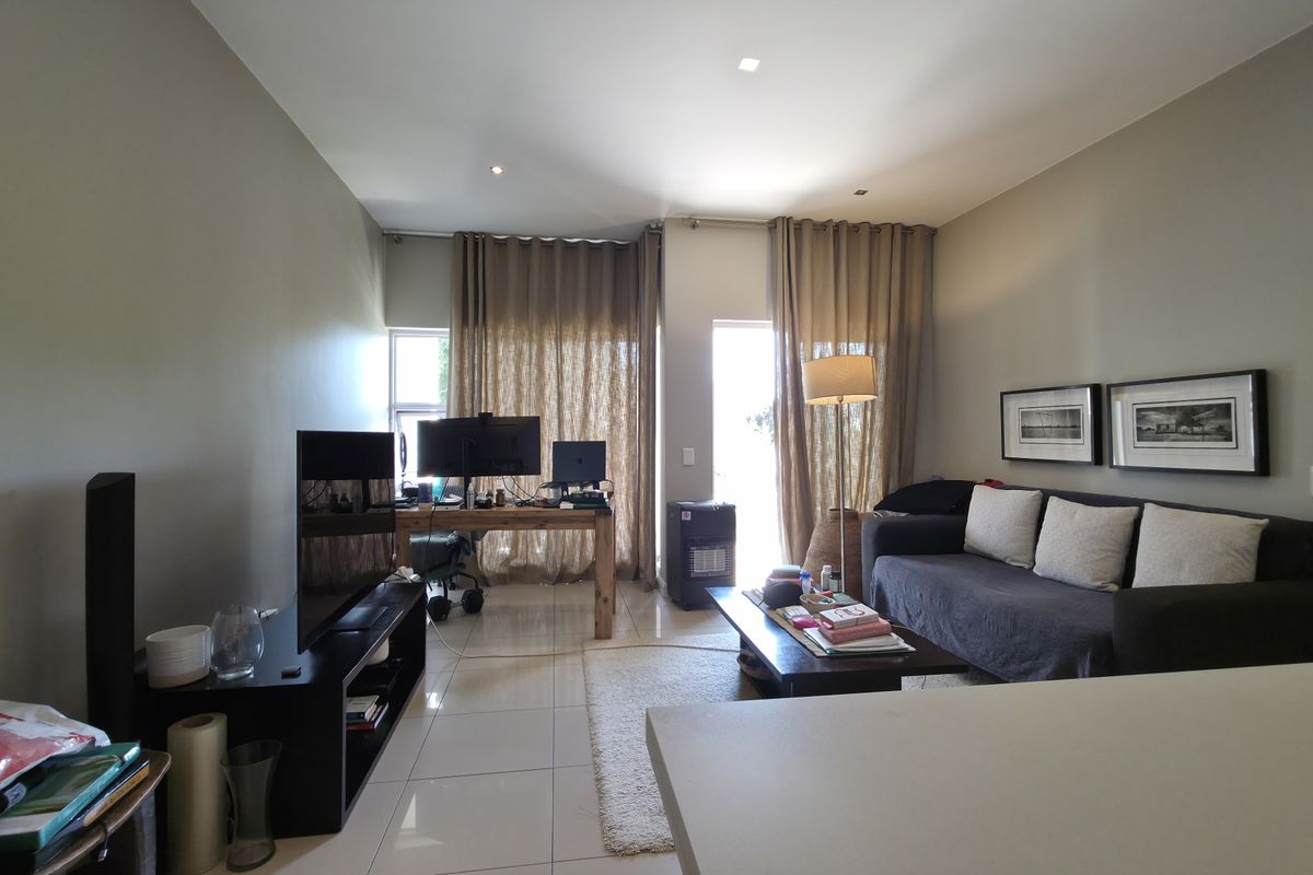 A spacious living area featuring neutral wall tones, large windows with floor-to-ceiling curtains, and polished tile flooring throughout.