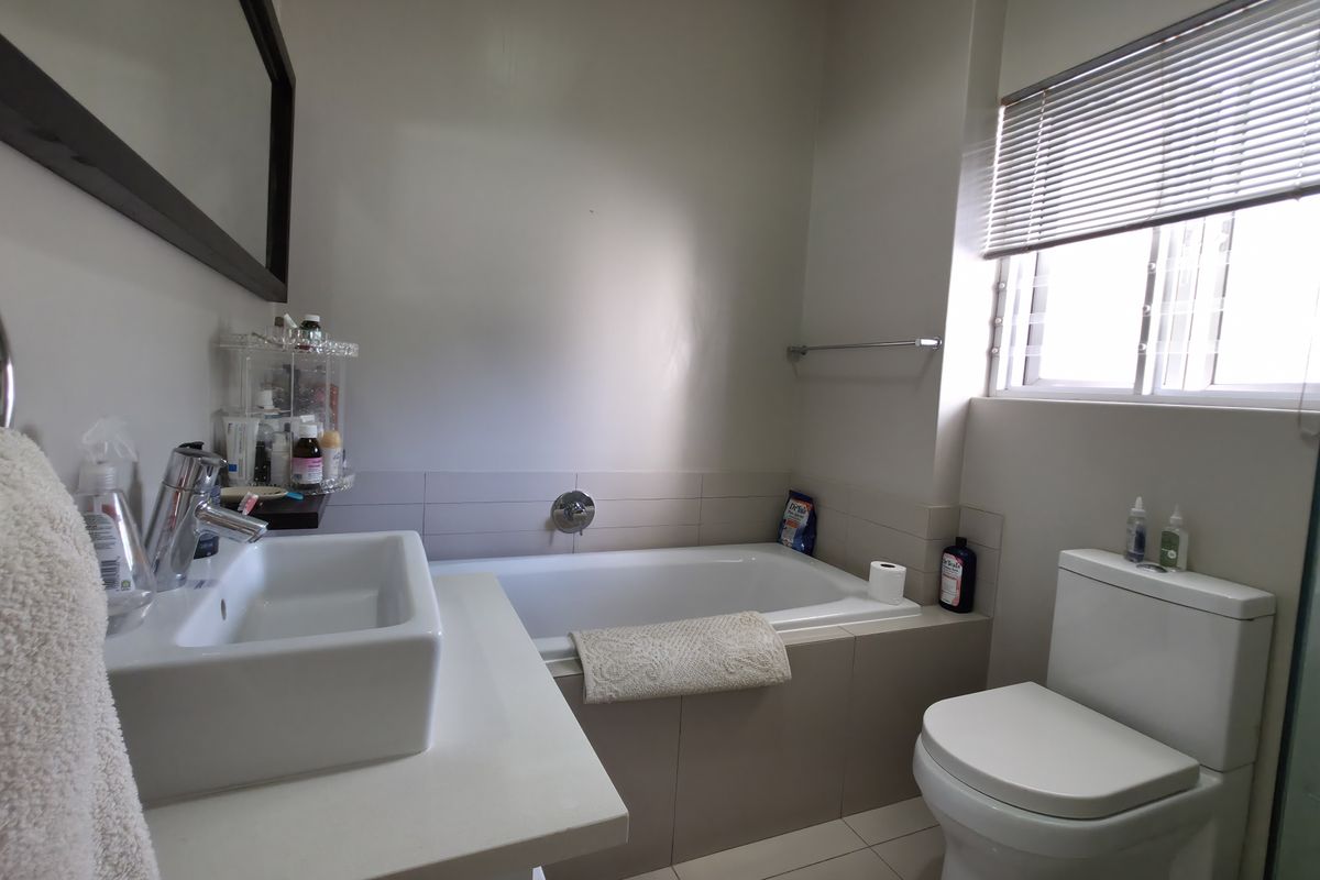 A functional bathroom featuring a built-in bathtub, modern vessel sink, and toilet, complemented by neutral wall tiles and natural light from the window.