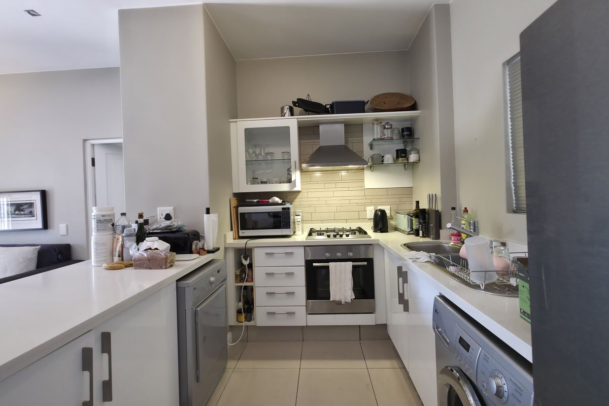 Compact modern kitchen featuring white cabinetry, stone countertops, tiled splashback, built-in oven, gas hob, and integrated laundry appliance space.