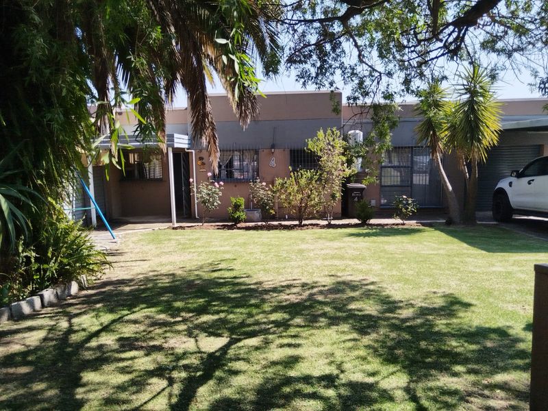 Front view of the apartment unit featuring a private lawn, security bars on windows, and an adjacent carport area.