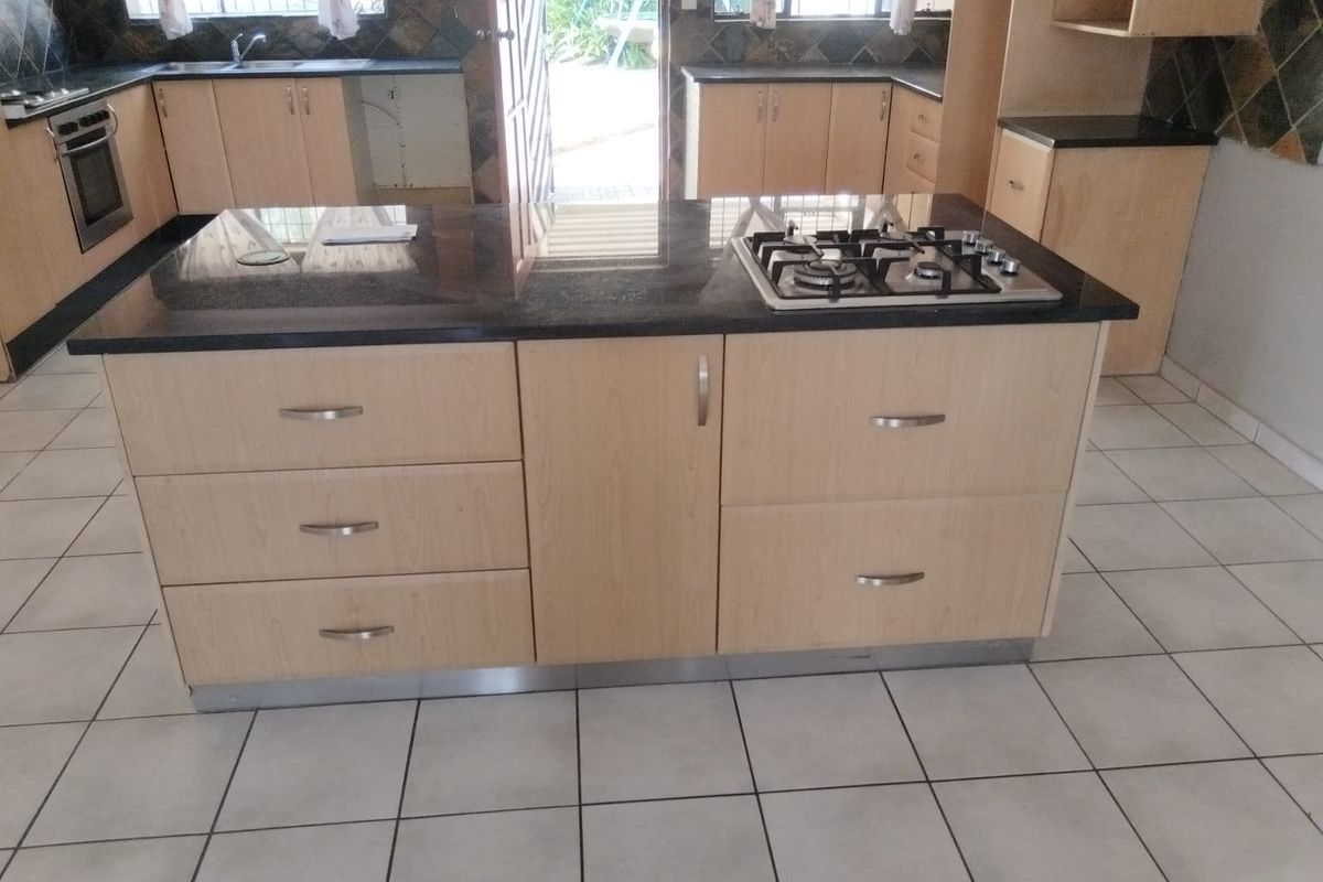 Spacious kitchen featuring a central island with a built-in gas hob, granite countertops, light wood cabinetry, and ceramic tiled flooring.