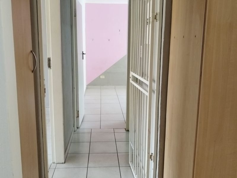 A functional hallway featuring tiled flooring, built-in cupboards, and a security gate, leading into an adjacent room with two-tone wall paint.